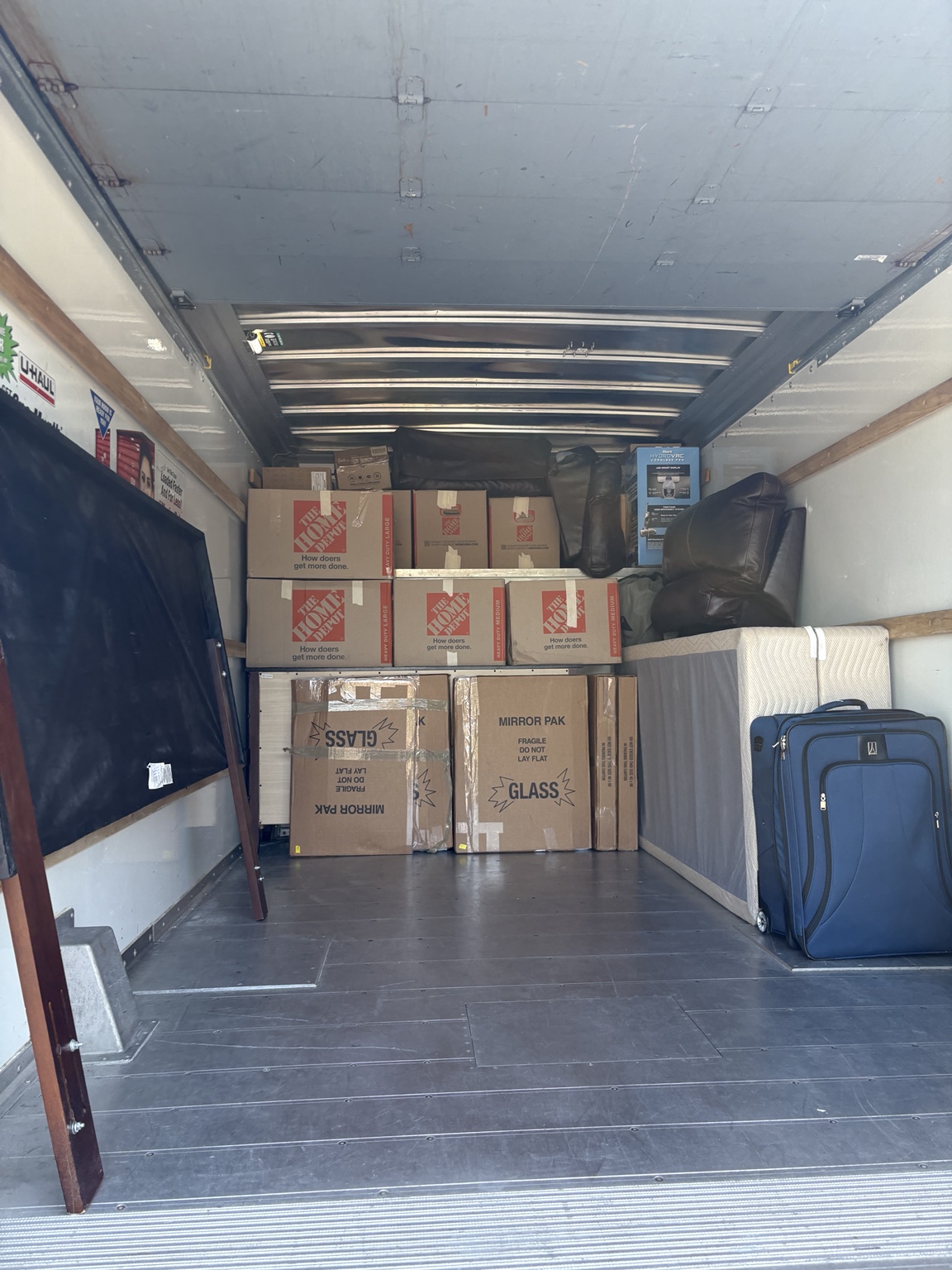 Stacked moving boxes, mirror cartons, a covered mattress and luggage inside a rental truck.