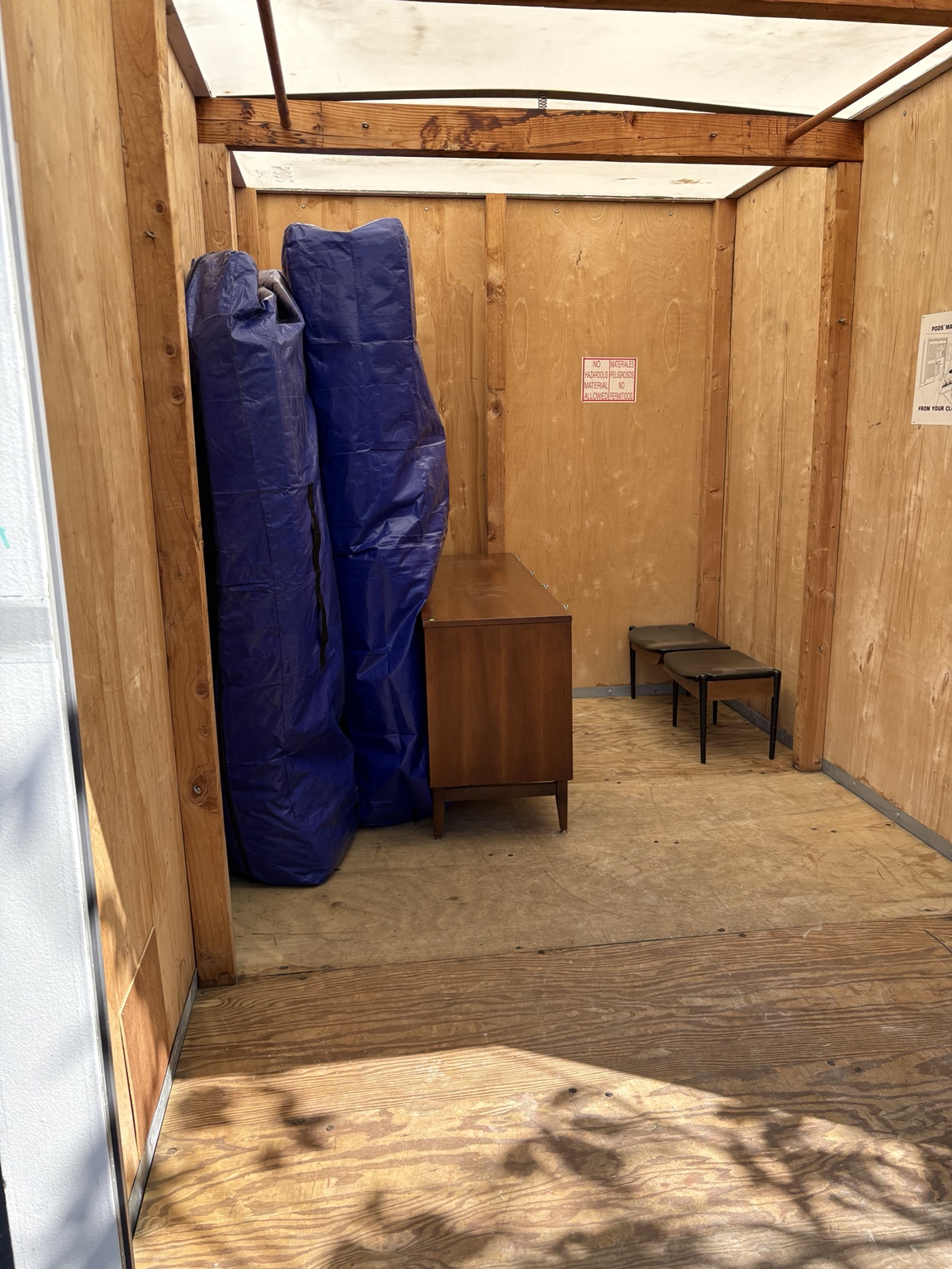 Blanket-wrapped furniture, a wooden cabinet and two stools inside a storage container.